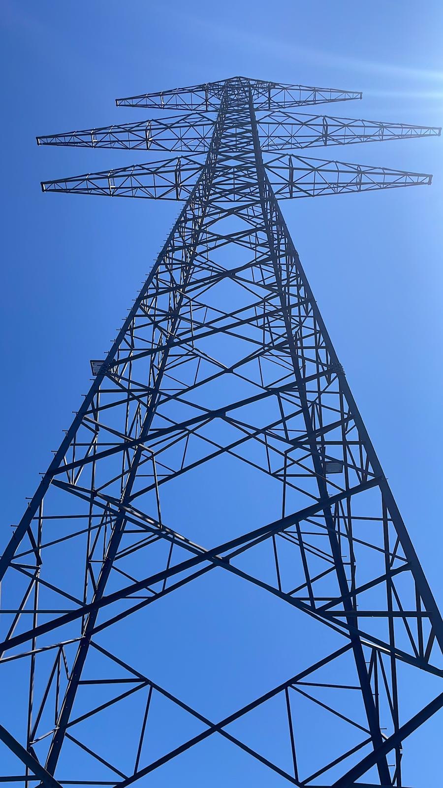 Słup kratowy linii 400 kV pod słońce na tle błękitnego nieba